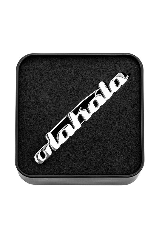 OLAKALA Pin mit silbernem Logo in einem schwarzen Feld, detaillierte Nahaufnahme des Designs, passend zum offiziellen OLAKALA® Onlineshop-Stil.