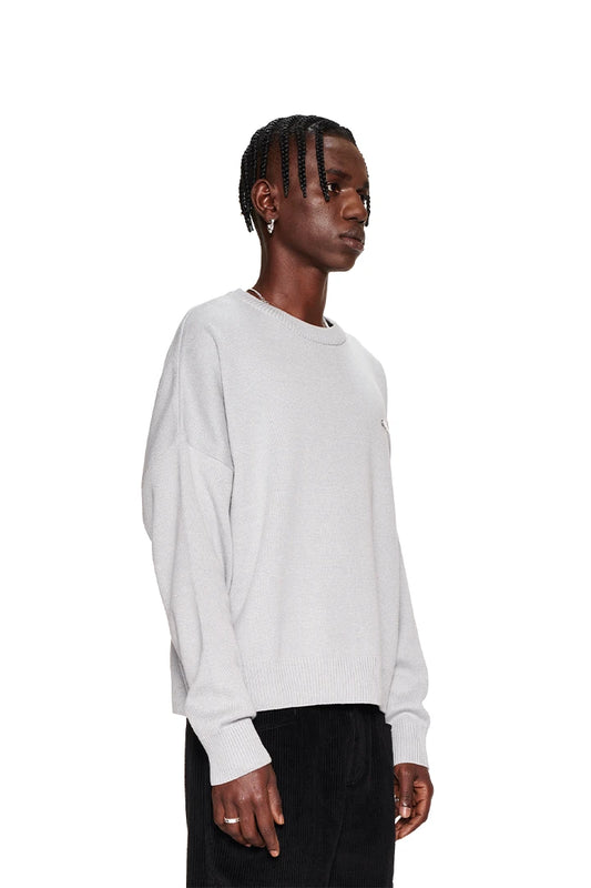 Mann in weißem CC Knit Sweater Gray mit überschnittenen Schultern und OLAKALA Pin, zeigt eine lässige, oversized Passform. Unisex-Design betont Mode und Komfort.