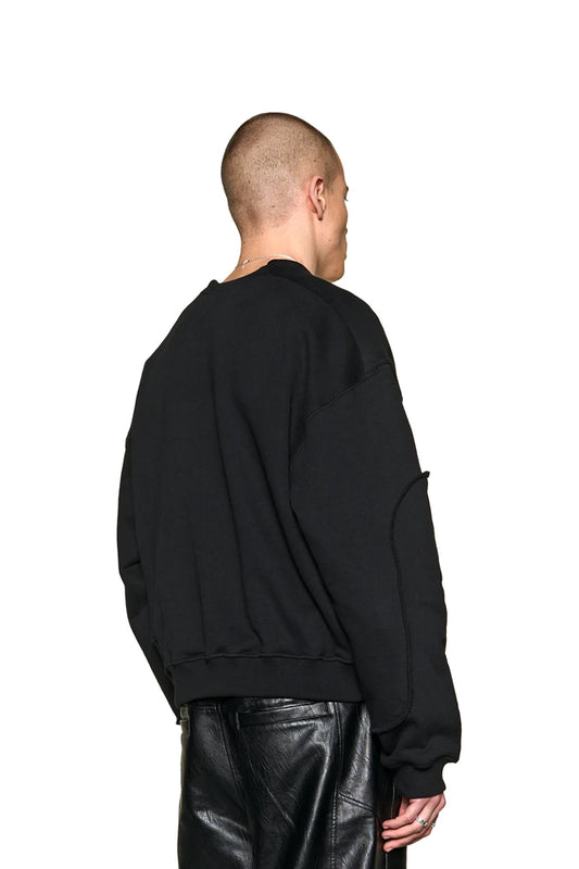 Man in the Defect ID Sweater Black by OLAKALA, oversized and unisex, features ribbed cuffs, dividing seams and digital print graphic on the chest.