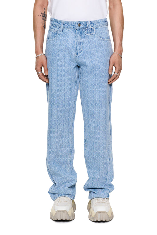 Person trägt CC Blue Monogram Denim Pants von OLAKALA mit versetztem Hosenbund und „Mittelfinger“ Patch, lockere Passform, sichtbar sind 5-Pocket-Design und geprägtes Patch.