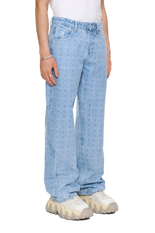 Person trägt CC Blue Monogram Denim Pants mit versetztem Hosenbund, 5-Taschen-Design, OLAKALA-Patch und lockerer Passform. Sichtbare Jeansdetails und Schuhe.