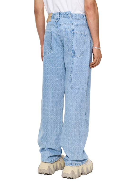 Person trägt CC Blue Monogram Denim Pants mit versetzten Nähten, 5-Taschen-Design und OLAKALA-Patch. Sichtbare Details: Hosentaschen, Gürtelschlaufen, lockere Passform.