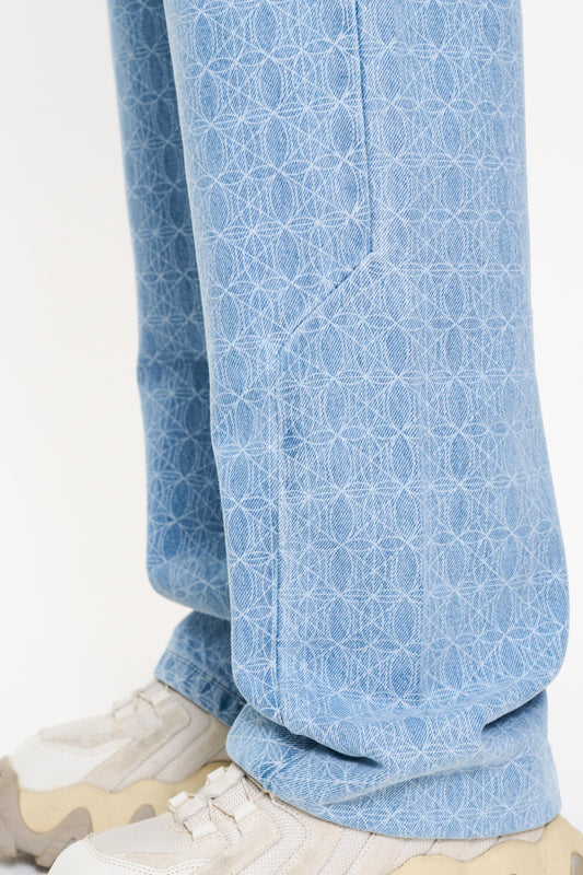 Person trägt CC Blue Monogram Denim Pants mit All-Over-Monogramm und lockerer Passform, kombiniert mit weißen Sneakers.