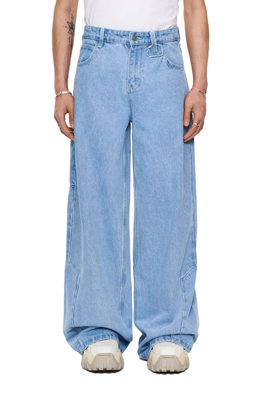 Person wears CC Blue Denim Pants Baggy with offset waistband, unisex design, very loose fit, OLAKALA patch and jeans button.