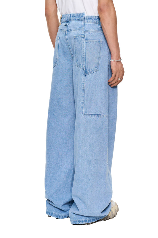 Person wears CC Blue Denim Pants Baggy with offset waistband and OLAKALA patch; unisex, loose fit, 14 oz denim fabric.