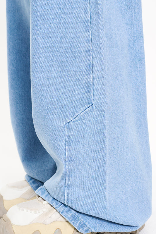 Close-up of CC Blue Denim Pants Baggy, showing 5-pocket design and staggered seams, worn with white sneakers.