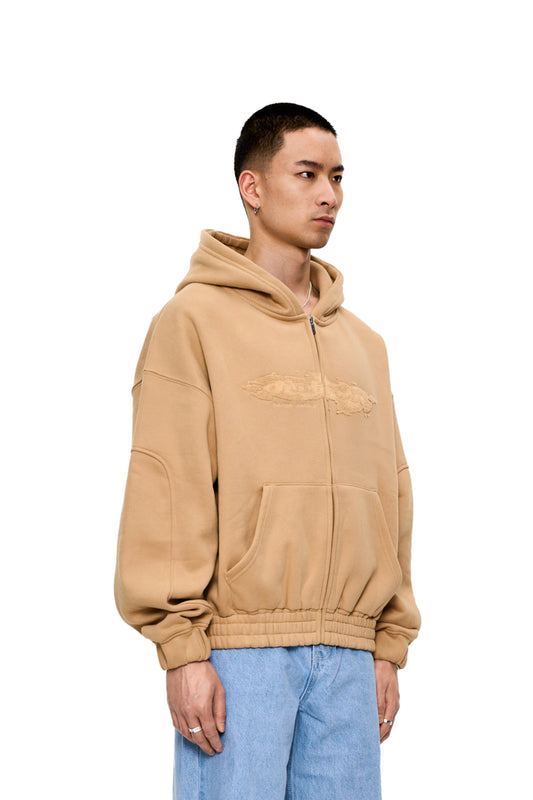 Mann in brauner OLAKALA CC Zip Hoodie Beige mit Reißverschluss, Kängurutasche, elastischen Bündchen und Frottee-Logo auf der Brust, oversized und unisex.