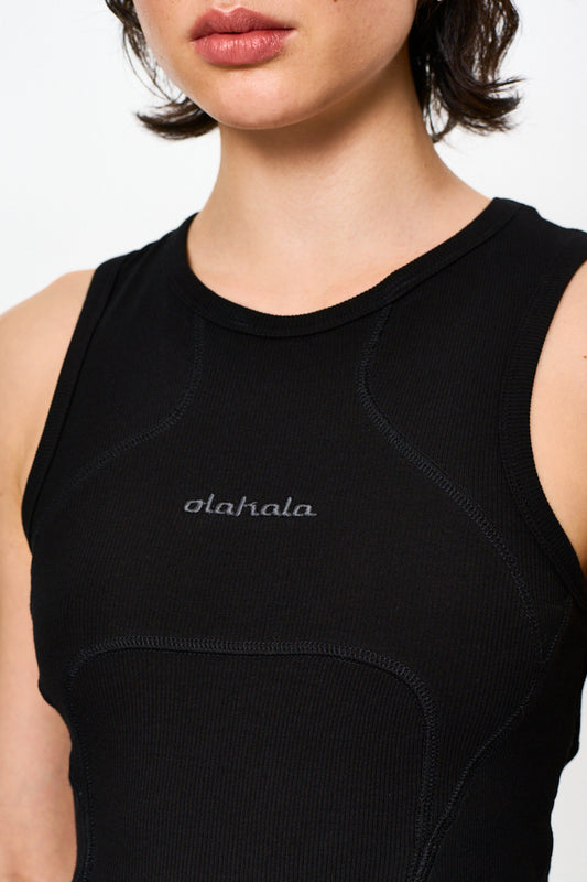 Nahaufnahme einer Frau, die das CC Anatomy Tanktop Cropped Black trägt, mit Ziernähten und gesticktem OLAKALA Logo vorne, eng anliegend und ärmellos.
