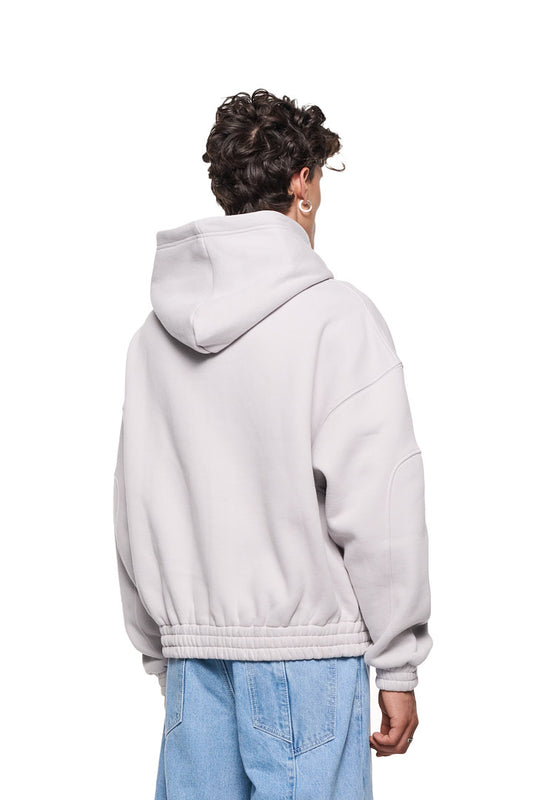 Person trägt Elysium Zip Hoodie Light Gray mit 2-Wege-Reißverschluss, Teilungsnähten an Ärmeln, Eingriffstaschen und elastischen Bündchen. Oversized Passform, unisex Design.