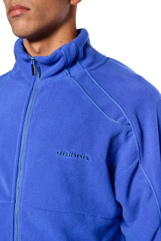 Nahaufnahme einer Fleecejacke Dazzling Blue mit gesticktem OLAKALA-Logo, Teilungsnähten, Eingriffstaschen und elastischen Bündchen.