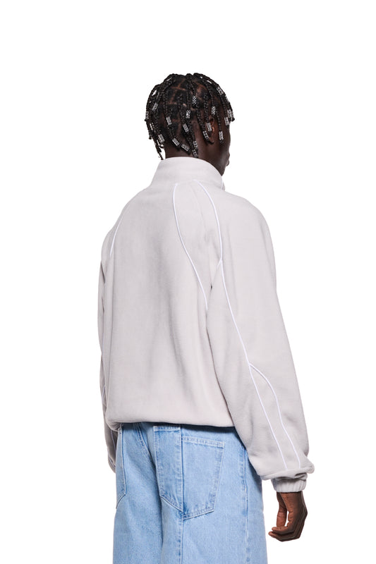 Person trägt eine weiße Fleecejacke Lunar Rock von OLA KALA mit Sticklogo, Teilungsnähten und Eingriffstaschen, oversized Unisex-Design, zeigt Ärmel und Hose.
