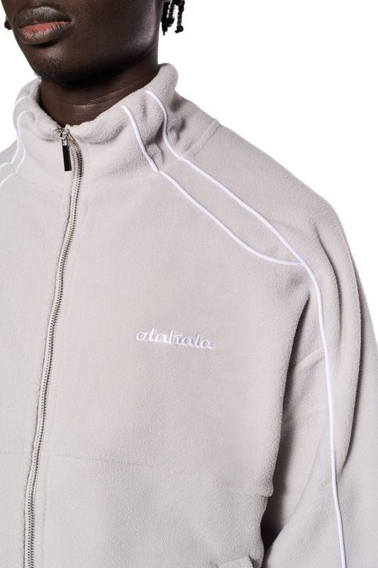 Nahaufnahme einer Fleecejacke mit OLA KALA-Logo-Stickerei auf der linken Brust, Teilungsnähten und Eingriffstaschen, oversized Unisex-Design.