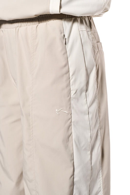 Nahaufnahme der Sports Tracksuit Pants Sand mit Reißverschlusstaschen und elastischem Kordelzug. OLAKALA-Logo auf der Gesäßtasche, unisex und robustes Rip-Stop Gewebe.