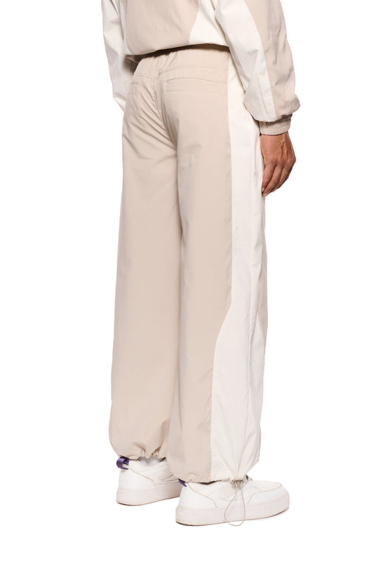 Person trägt die Sports Tracksuit Pants Sand mit elastischem Kordelzug und Reißverschlusstaschen, erkennbar an gesticktem OLAKALA Sports Icon und Logo.