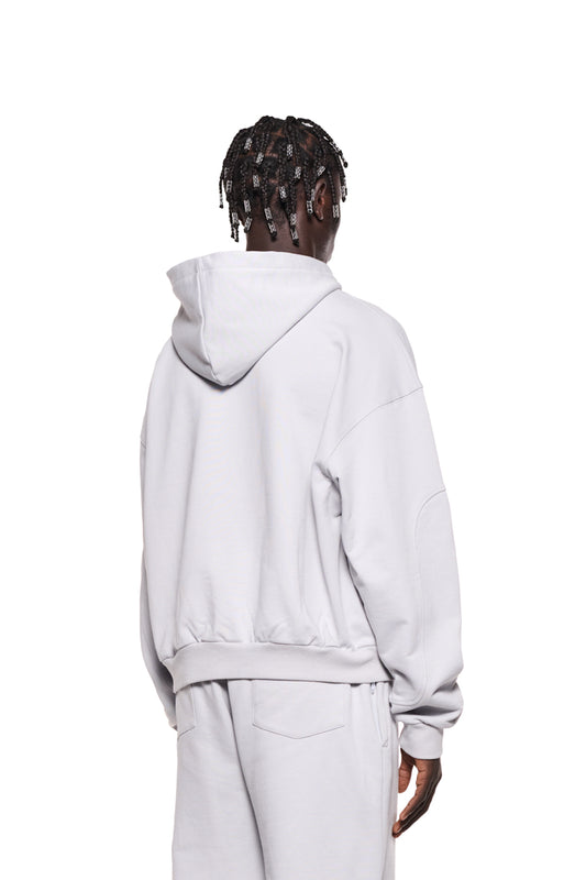 Person trägt grauen Sports Hoodie mit Teilungsnähten und Ripp-Bündchen. Gestickte OLAKALA Sports Grafik auf der Brust, oversized Unisex Design.