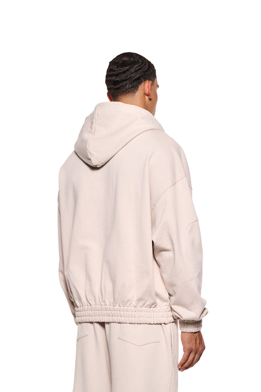 Ein Mann trägt einen Sports Zip Hoodie Beige mit 2-Wege-Reißverschluss, elastischen Bündchen und gestickter OLAKALA Sports Grafik auf der Brust, oversized Unisex-Passform.