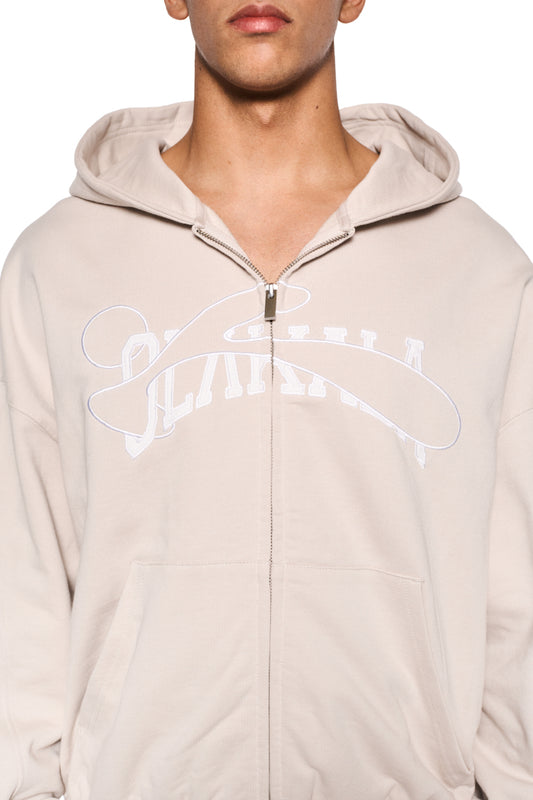 Person trägt einen Sports Zip Hoodie Beige mit 2-Wege-Reißverschluss, Teilungsnähten und gestickter OLAKALA Sports Grafik auf der Brust, oversized Passform.