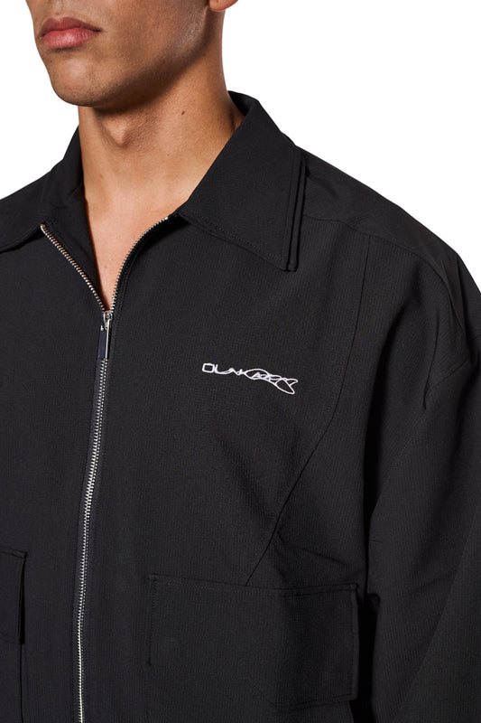 Synergy Ripstop Jacke Schwarz, Nahaufnahme: Zipper-Detail, doppelte Kragen, gesticktes Synergy-Logo auf Brust, robuste Nähte, elastische Bündchen, Cargo-Taschen mit Magnetverschluss.