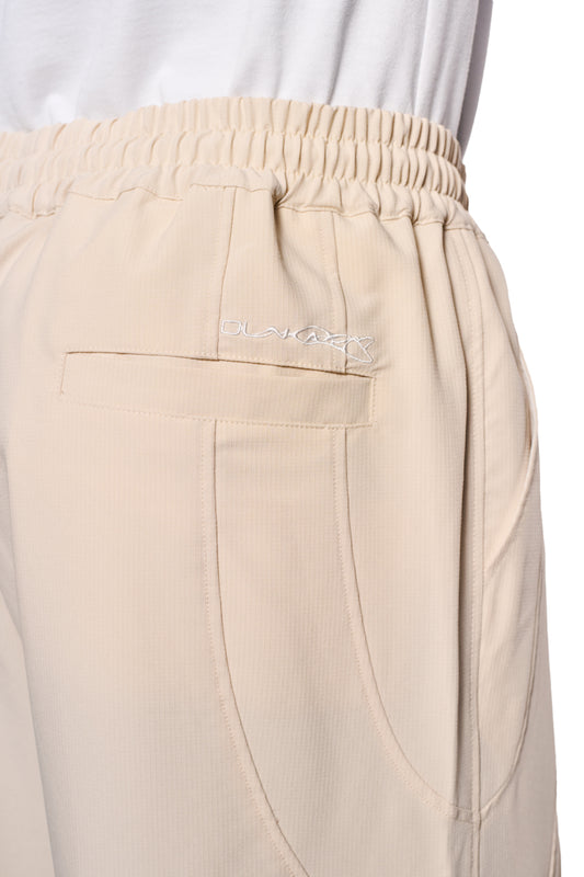 Nahaufnahme der Synergy Cargo Pants Sand mit robustem Rip-Stop Gewebe, Kordelzug, Cargo- und Leistentaschen sowie gesticktem Synergy-Logo über der Gesäßtasche.