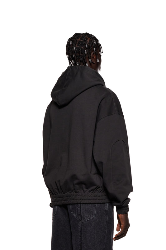 Person wearing Synergy Zip Hoodie Black with 2-way zipper, dividing seams on sleeves, Synergy logo on chest, oversized and unisex design.