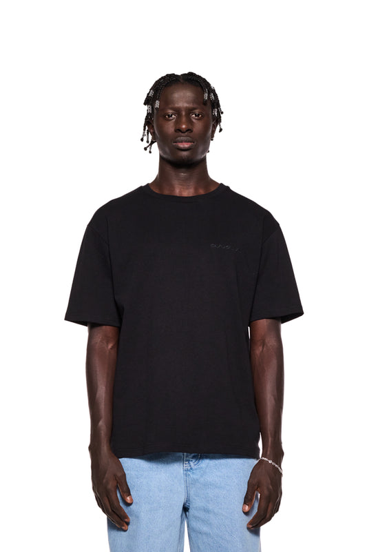 Mann trägt NC T-Shirt Black Regular mit OLA KALA Logo auf der Brust und Grafik auf dem Rücken. Unisex, Regular Fit, aus EU-Produktion.