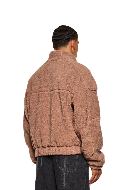 Mann trägt Teddy Jacket Brown mit hohem Kragen, Teilungsnähten, Eingriffstaschen und gesticktem OLAKALA-Logo. Sichtbar: Rückseite, Ärmel, Handtasche.