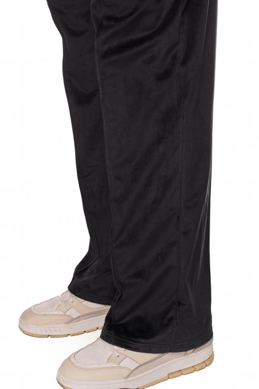 Beine in schwarzen Sports Velour Jogger Pants mit lockerer Passform, offenen Beinabschlüssen und seitlichen Eingriffstaschen; gesticktes OLAKALA Sports Icon sichtbar.