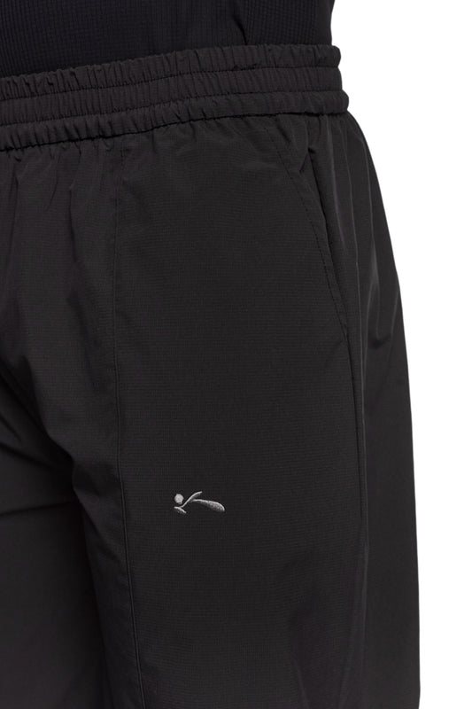 Nahaufnahme von OLAKALA Sports Trackpants in Schwarz mit sportlichen Kontrasteinsätzen, elastischem Bund und gesticktem Logo auf dem linken Bein.