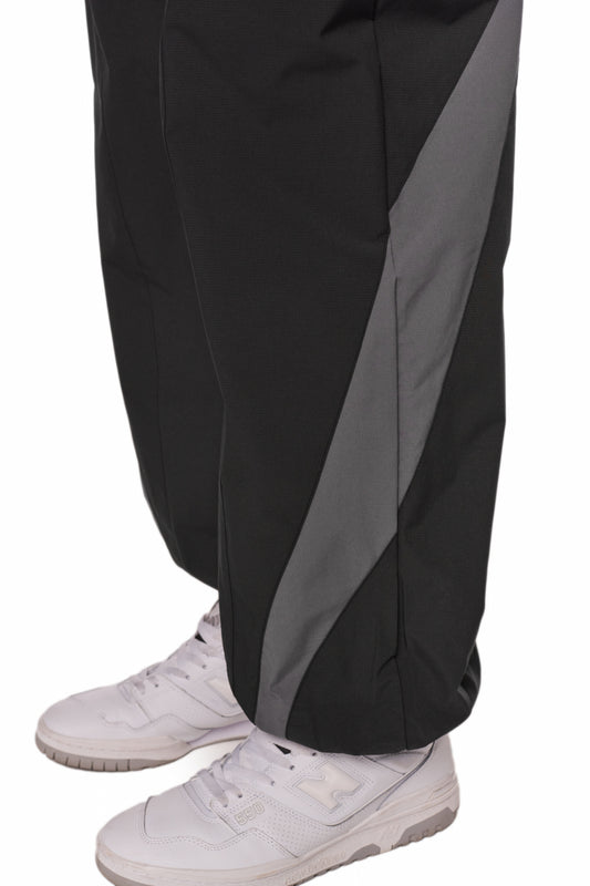 Person trägt Sports Trackpants Black, aus robustem Rip-Stop Gewebe mit OLAKALA Logo, kombiniert mit weißen Sneakers für sportlichen Look.