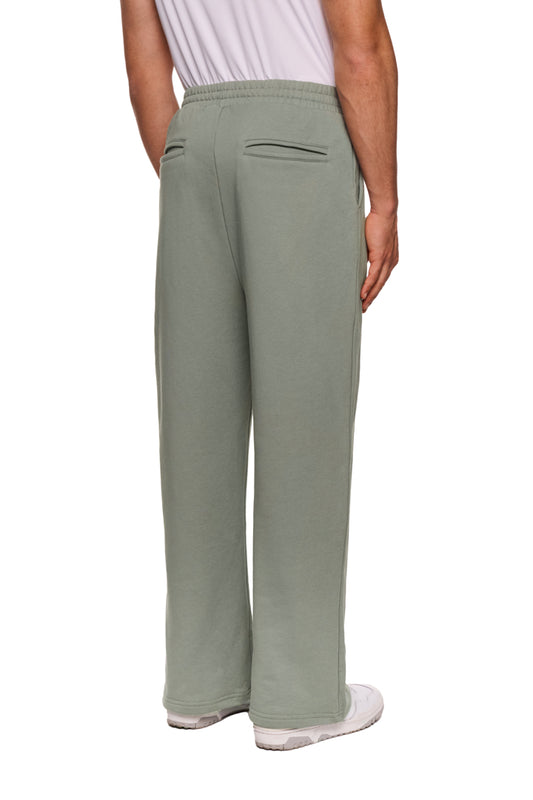 Eine Person trägt die Sports Loose Fit Sweatpants mit Händen in den Taschen, elastischem Bund und gesticktem OLAKALA Sports Logo am linken Bein.