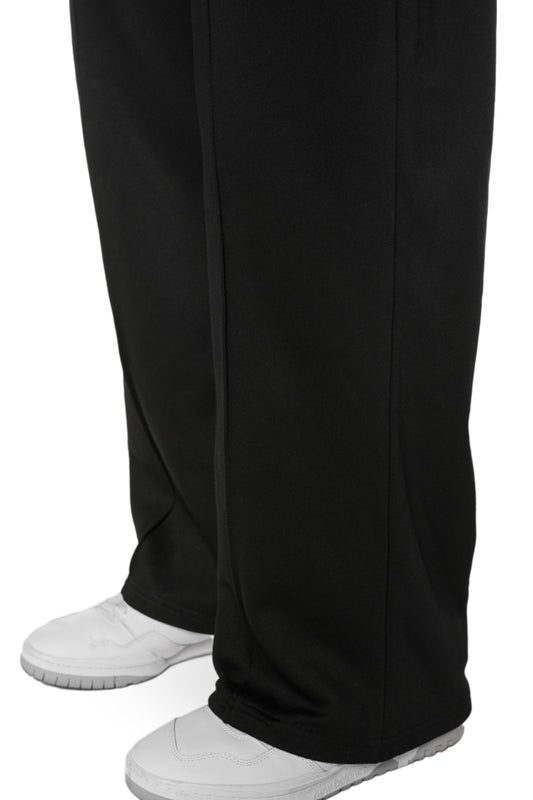 Person trägt OLAKALA Sports Loose Fit Sweatpants Black mit offener Beinabschluss, gesticktem Logo und elastischem Bund mit Kordelzug, zeigt Nahaufnahme der Schuhe.