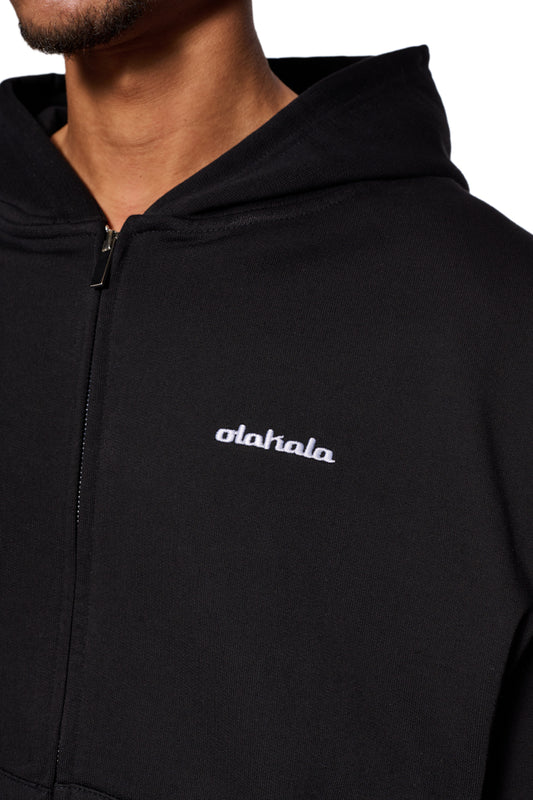 Person trägt CC Zip Hoodie Black mit gesticktem OLAKALA Logo, Zwei-Wege-Reißverschluss, elastischen Bündchen und oversized Unisex-Passform.