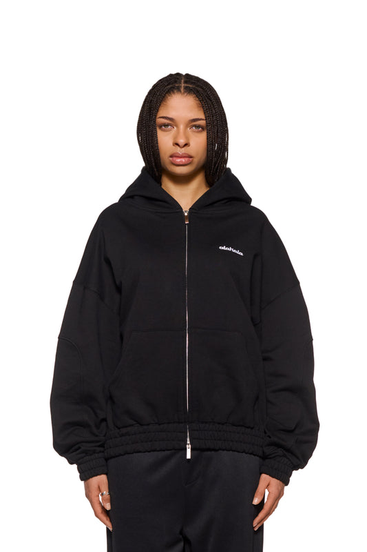 Frau trägt CC Zip Hoodie Black mit gesticktem OLAKALA Logo und elastischen Bündchen. Oversized und unisex, mit 2-Wege-Reißverschluss und Kapuze.