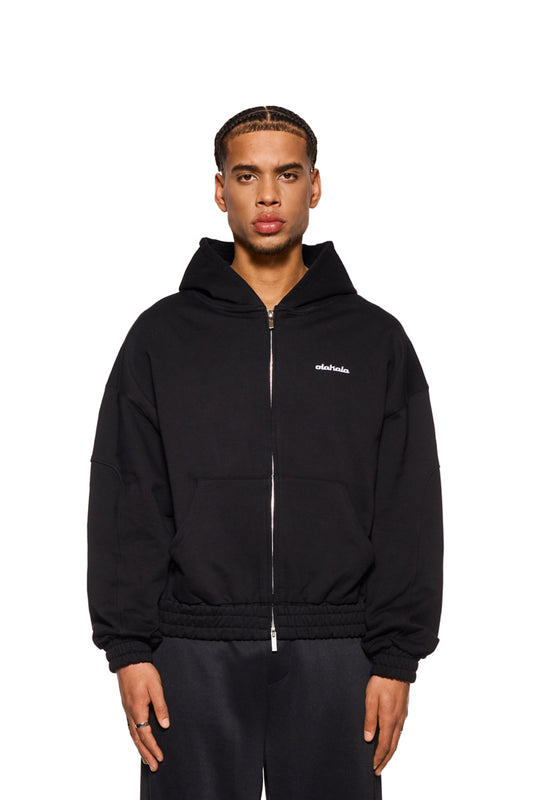 Mann trägt CC Zip Hoodie Black mit gesticktem OLAKALA Logo und elastischen Bündchen, zeigt oversized Passform und 2-Wege-Reißverschluss.
