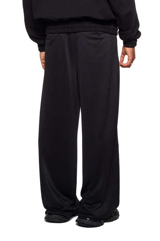 Person trägt CC Jogger Pants Black mit elastischem Bund und Kordelzug, französischen Eingriffstaschen und gesticktem OLAKALA Logo, passend für einen lässigen, unisex Stil.
