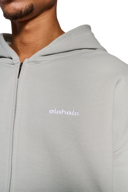Person trägt den CC Zip Hoodie Pussywillow Gray mit gesticktem OLAKALA-Logo, elastischen Bündchen und vorne mittigem 2-Wege-Reißverschluss in Oversized-Passform.