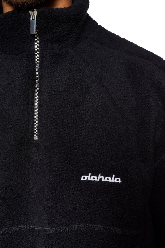 Nahaufnahme des CC Fleece Halfzip Black mit elastischen Bündchen, hohem Kragen und gesticktem OLAKALA-Logo auf der linken Brust.