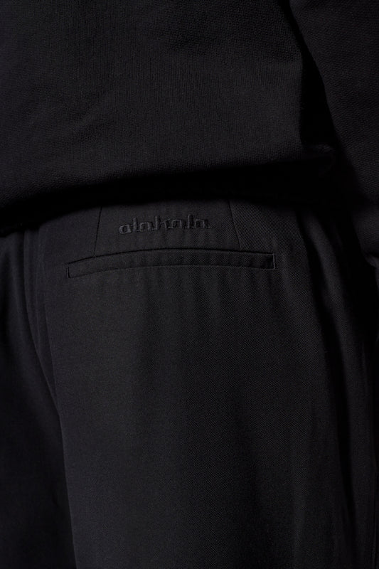 Nahaufnahme der Gills Dress Pants von OLAKALA mit französischen Taschen, asymmetrischem Eingriff, Bundfalten und gesticktem Logo über der rechten Gesäßtasche.