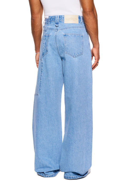 Person wears CC Blue Loose Fit Denim Pants with offset waistband and embroidered OLAKALA logo, emphasizing casual fit and unisex design.