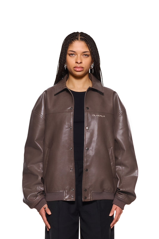 Frau trägt CC Leather Jacket Brown mit Reißverschluss, Druckknöpfen und gesticktem OLAKALA-Logo. Veganes Lederimitat, oversized Passform, unisex Design.