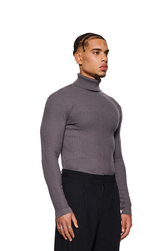 Mann trägt einen grauen Anatomy Turtleneck von OLAKALA mit Rollkragen und eng anliegender Passform, präsentiert in einem lässigen Stil.