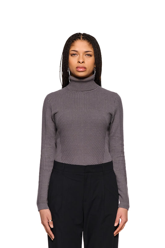 Frau trägt Anatomy Turtleneck Gray mit Rollkragen und engem Schnitt aus der OLAKALA-Kollektion. Strickpullover zeigt verschiedene Strickmuster.