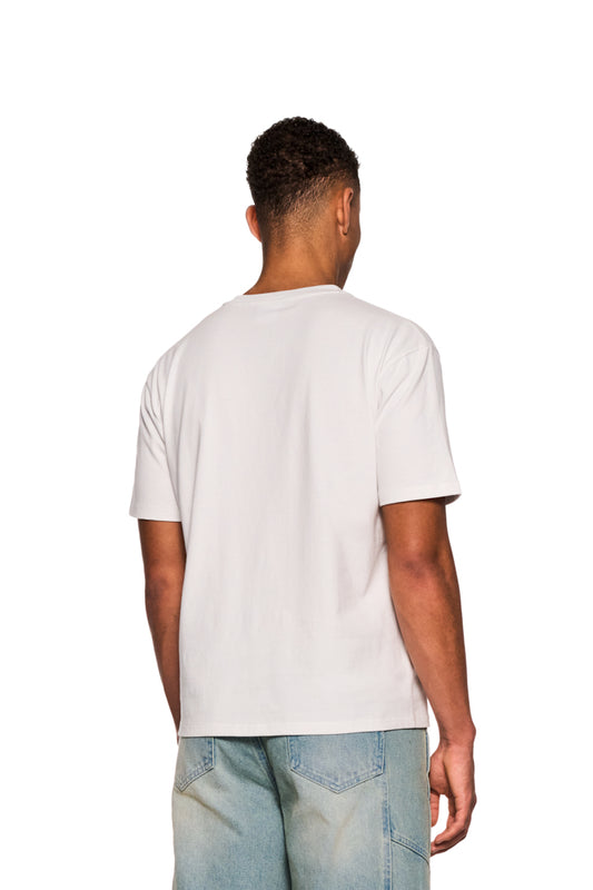 Mann trägt E.O.I. T-Shirt White mit Ripp-Kragen und Siebdruck-Grafik. Nahaufnahme von Jeans im Hintergrund. Unisex, reguläre Passform.