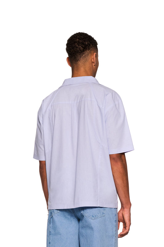 Mann trägt Layered Short Sleeve Shirt Blue mit kubanischem Kragen, Knopfleiste, Brusttaschen und gesticktem OLAKALA Logo, Rückennaht sichtbar.