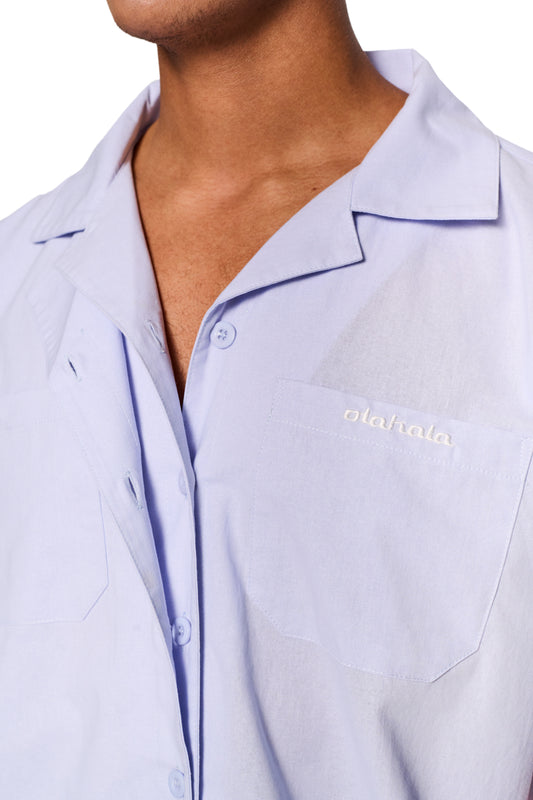 Nahaufnahme des Layered Short Sleeve Shirt Blue mit kubanischem Kragen, Knopfleiste und gesticktem OLAKALA-Logo auf der Brusttasche. Unisex, lockere Passform.