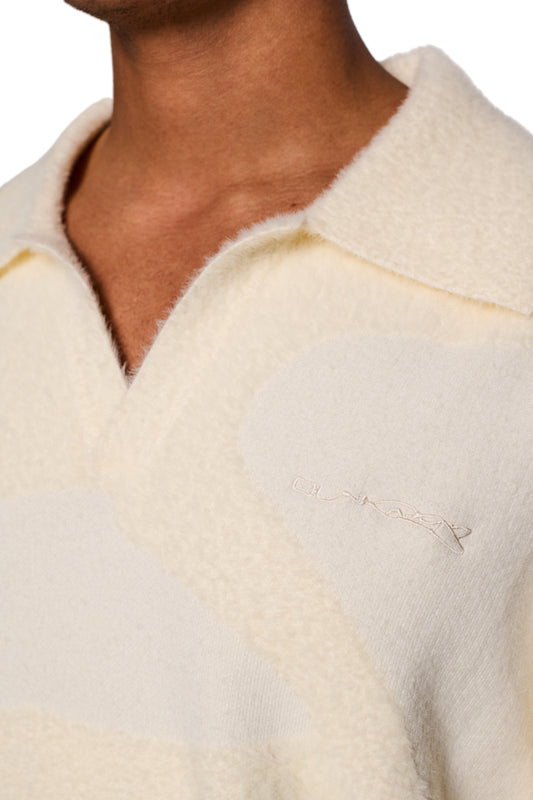 Person trägt den Glitched Fuzzy Polo Cream mit Polokragen, gerippten Bündchen und gesticktem Synergy-Logo auf der Brust, präsentiert von OLAKALA.