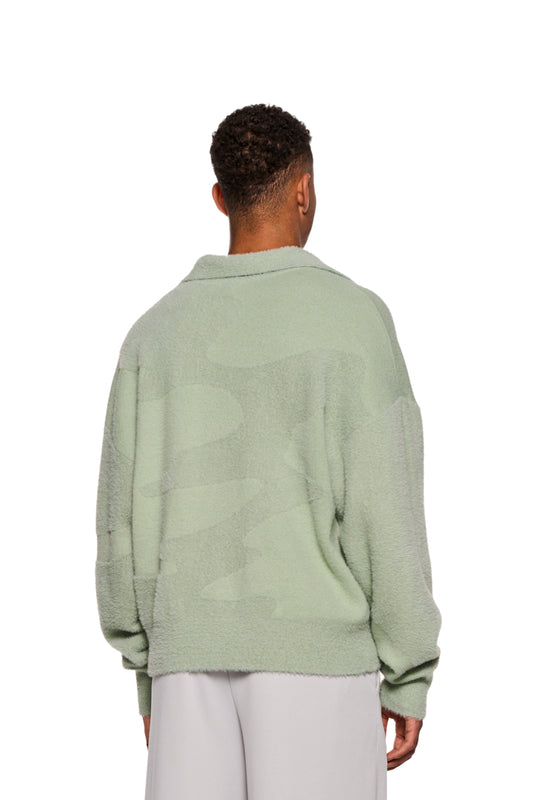 Person in green glitched fuzzy polo mint with polo collar and embroidered Synergy logo on the chest, unisex, regular fit, made of fluffy material.