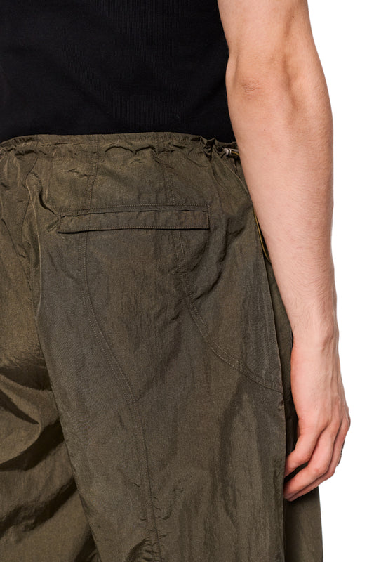 Nahaufnahme einer Person, die die Parachute Pants Khaki von OLAKALA trägt, mit sichtbaren Eingriffstaschen und Paspeltaschen-Details am Rücken.