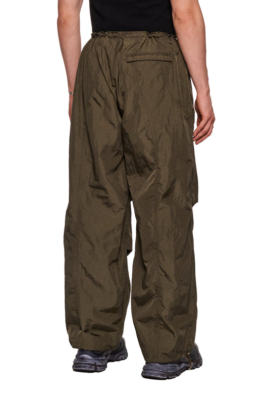 Person in Khaki-Parachute-Hose mit elastischem Kordelzug und gesticktem Synergy-Logo, lockerem Schnitt, seitlichen Eingriffstaschen und Paspeltasche hinten.