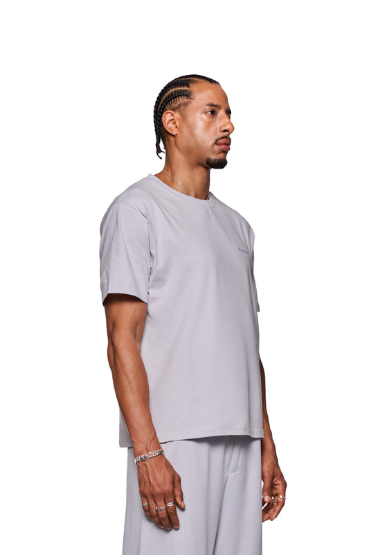 Mann im weißen Shirt mit gesticktem OLAKALA Logo auf der Brust, trägt silberne Ringe und Armband. CC T-Shirt Regular Gray von OLAKALA.